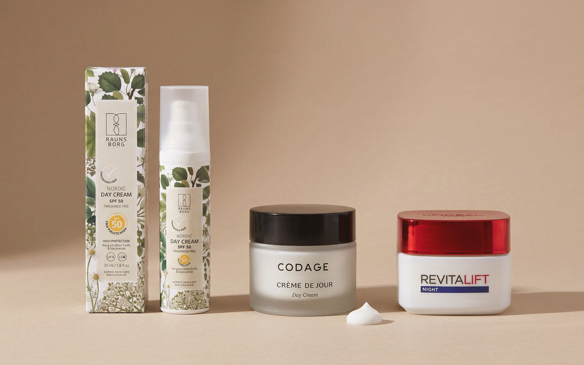Raunsborg Day Cream SPF 50 Parfumefri, CODAGE Crème de Jour og L'Oréal Paris Revitalift Classic Natcreme på sand baggrund