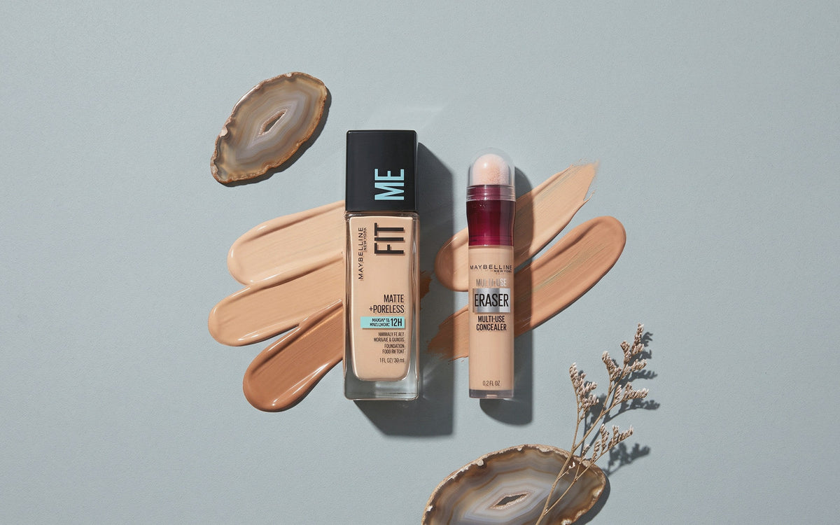 Maybelline Fit Me Matte + Poreless foundation ved siden af en Instant Age Rewind concealer på gråblå baggrund