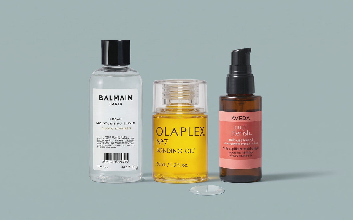 Balmain Paris Argan Moisturizing Elixir, Olaplex No. 7 Bonding Oil og Aveda Nutriplenish Multi-Use Hair Oil på gråblå baggrund