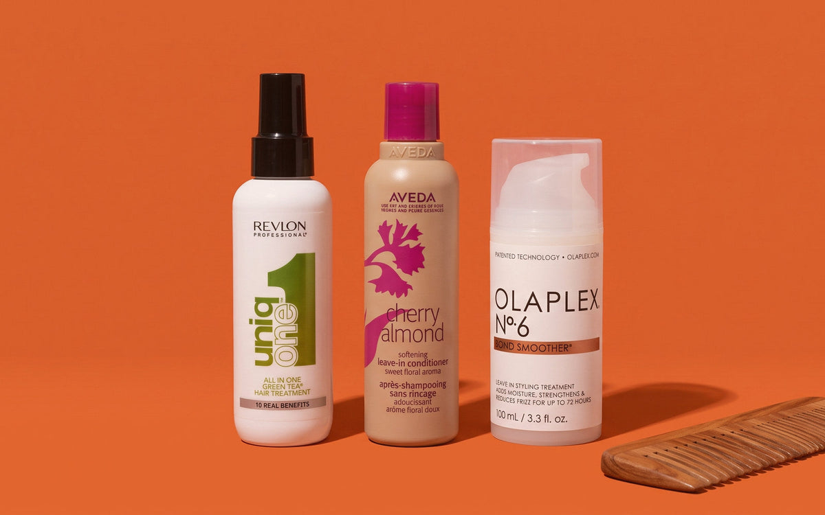 Revlon Professional Uniq One All In One Hair Treatment, Aveda Cherry Almond Softening Leave-In Conditioner og Olaplex No. 6 Bond Smoother på orange baggrund