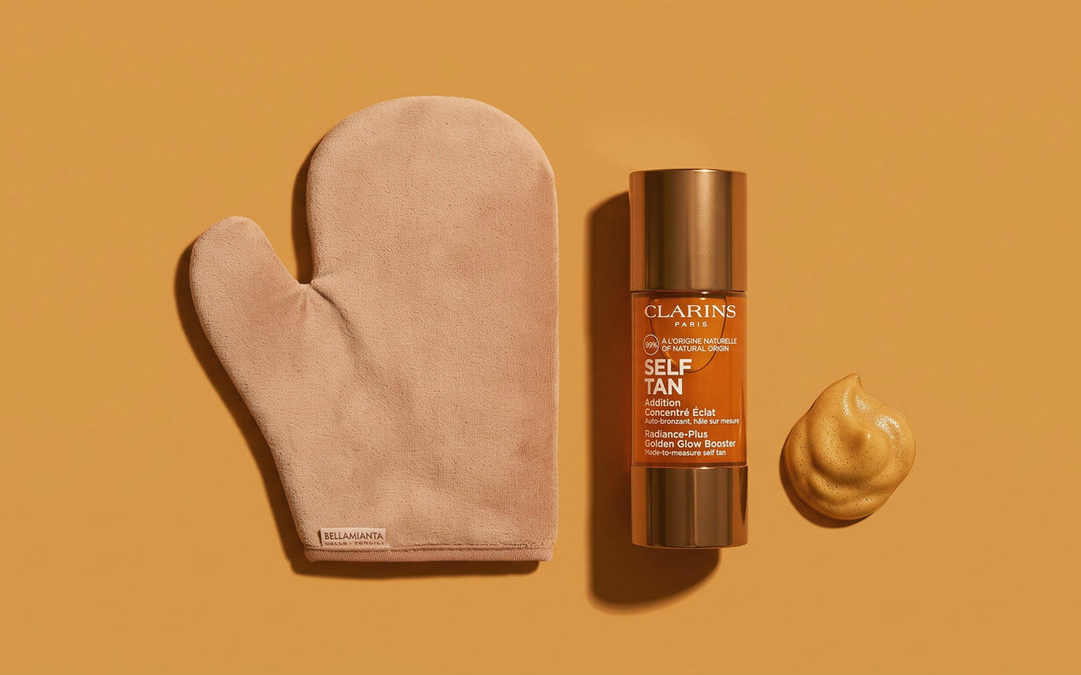 Bellamianta selvbruner-handske ved siden af Clarins Self Tan Golden Glow Booster på okkerfarvet baggrund