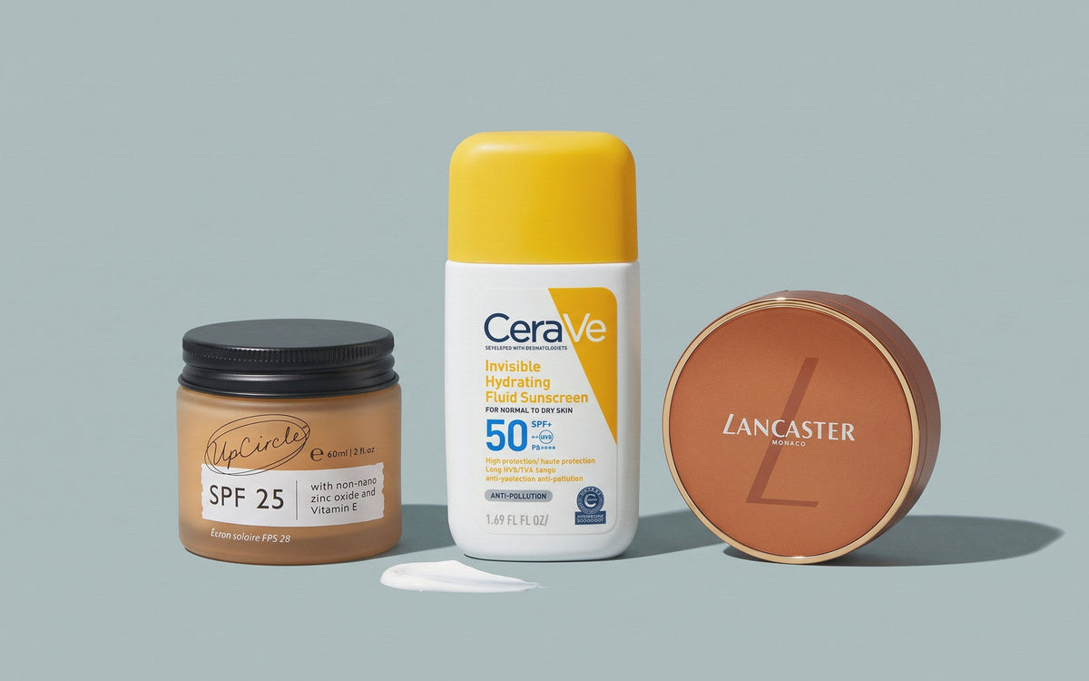 UpCircle SPF 25 Mineralsk Solcreme, CeraVe Invisible Hydrating Fluid Sunscreen SPF50 og Lancaster Sun Infinite Bronze Compact Cream SPF50 på gråblå baggrund