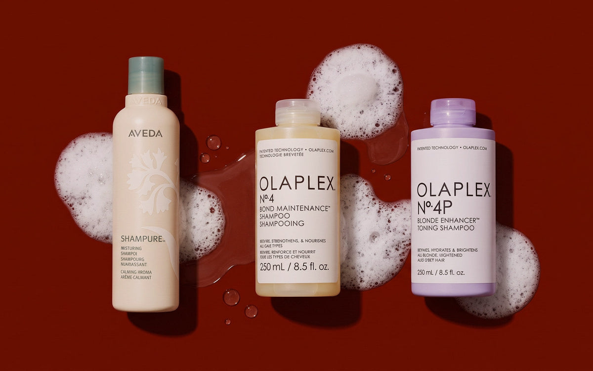Aveda Shampure shampoo ved siden af Olaplex No. 4 og Olaplex No. 4P på mørk rødbrun baggrund